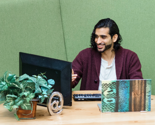 Man at desk interacts with secondary computer monitor on a video call.