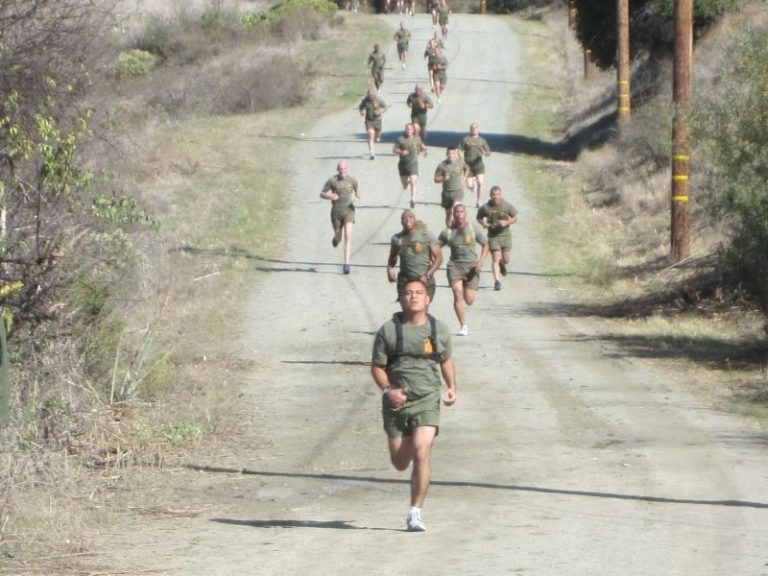 Marines run down a dusty road on a military base