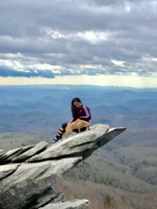 Florabel sitting on a scenic cliffside with a dog. 