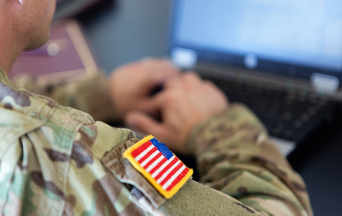 Over-the-shoulder photograph of service member working on laptop
