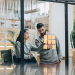 Businessman discussing with businesswoman sticking adhesive notes on glass wall in office M2