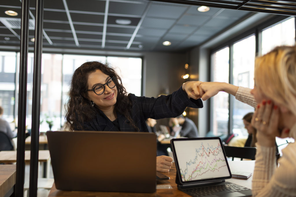 Female coworkers doing fist bump over laptop screens