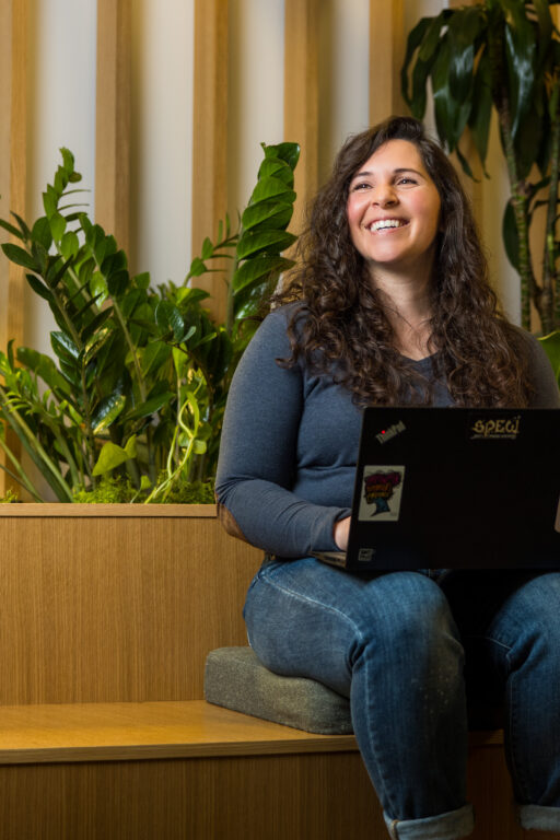 Woman in blue jeans smiles with laptop on her lap.