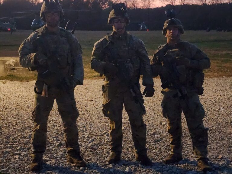 Three soldiers face the camera with the sun behind them